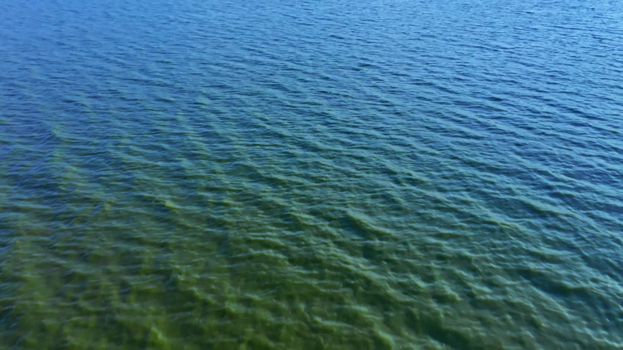 Calm aerial drone footage of a serene English lake with gentle ripples and expansive blue sky. Captivating water textures under natural sunlight create a peaceful atmosphere