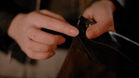 Woman-hands-using-a-burnishing-tool-on-black-leather-in-the-workshop,-dark-setup,-high-contrast,-color-graded