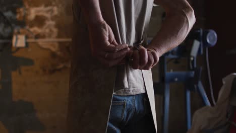 Midsection-of-caucasian-male-blacksmith-wearing-apron-in-workshop