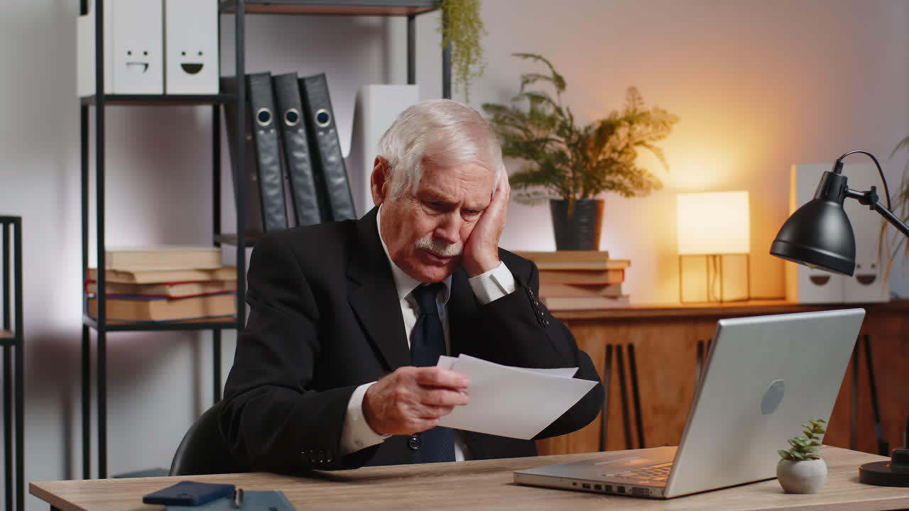 Senior businessman opening envelope reading bad news in letter feels upset sitting at office desk
