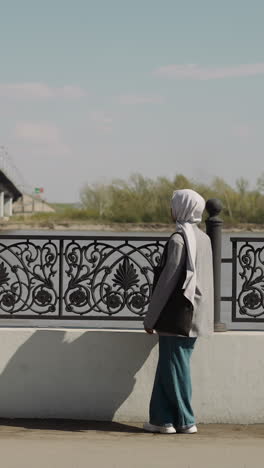arabian black woman with chiffon headscarf enjoys river view on city waterfront. african-american lady with muslim accessory in town. tourism and vacation