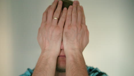 close up of young man's face looking desperately into the camera and covers his face with his hands