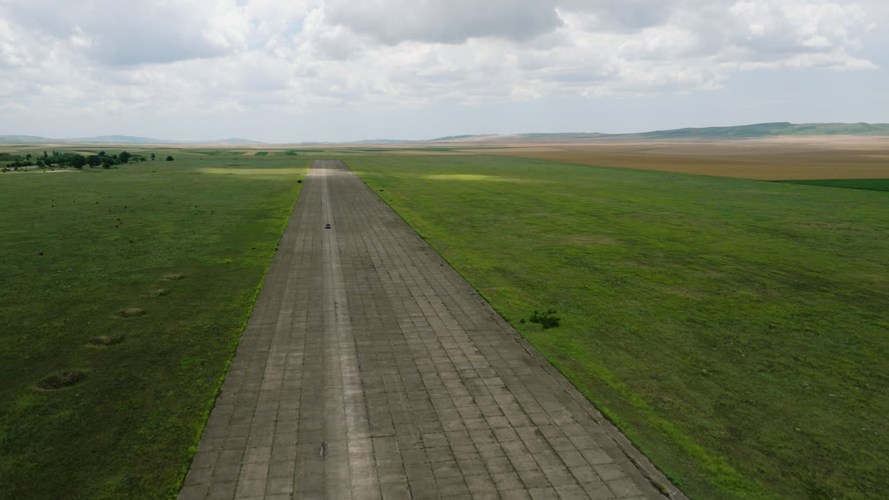 автомобиль едет по широкой асфальтированной взлетно-посадочной полосе военного аэродрома сираки