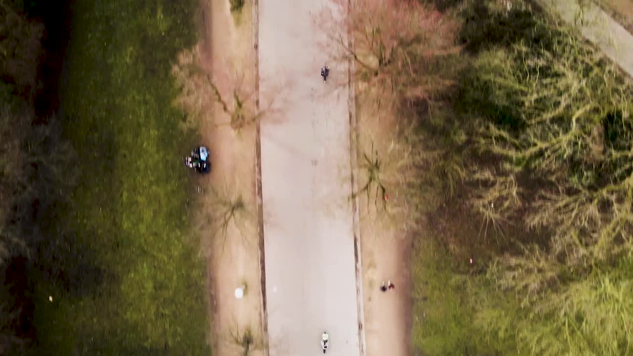 Persone che camminano e vanno in bicicletta in un parco con alberi spogli e aree verdi, vista aerea