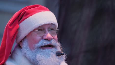 a positive old american santa claus speaks to the audience into microphone while standing on stage a positive old american santa claus speaks to the audience into a microphone while standing on stage new years santa claus wishes people a merry christmas makes emotional gestures new year party