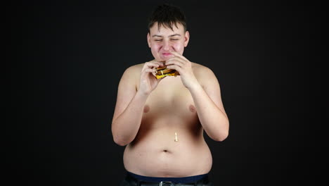 young overweight man eating burger naked to the waist, fast food and unhealthy diet concept