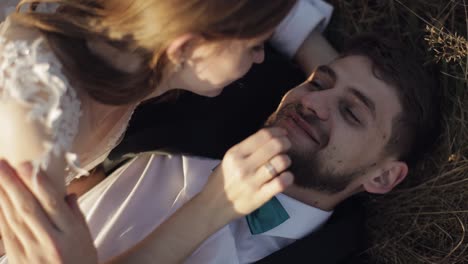 a bride and groom lying in a field, smiling at each other