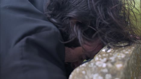 crying man mourning over death of loved one at grave tombstone in cemetery