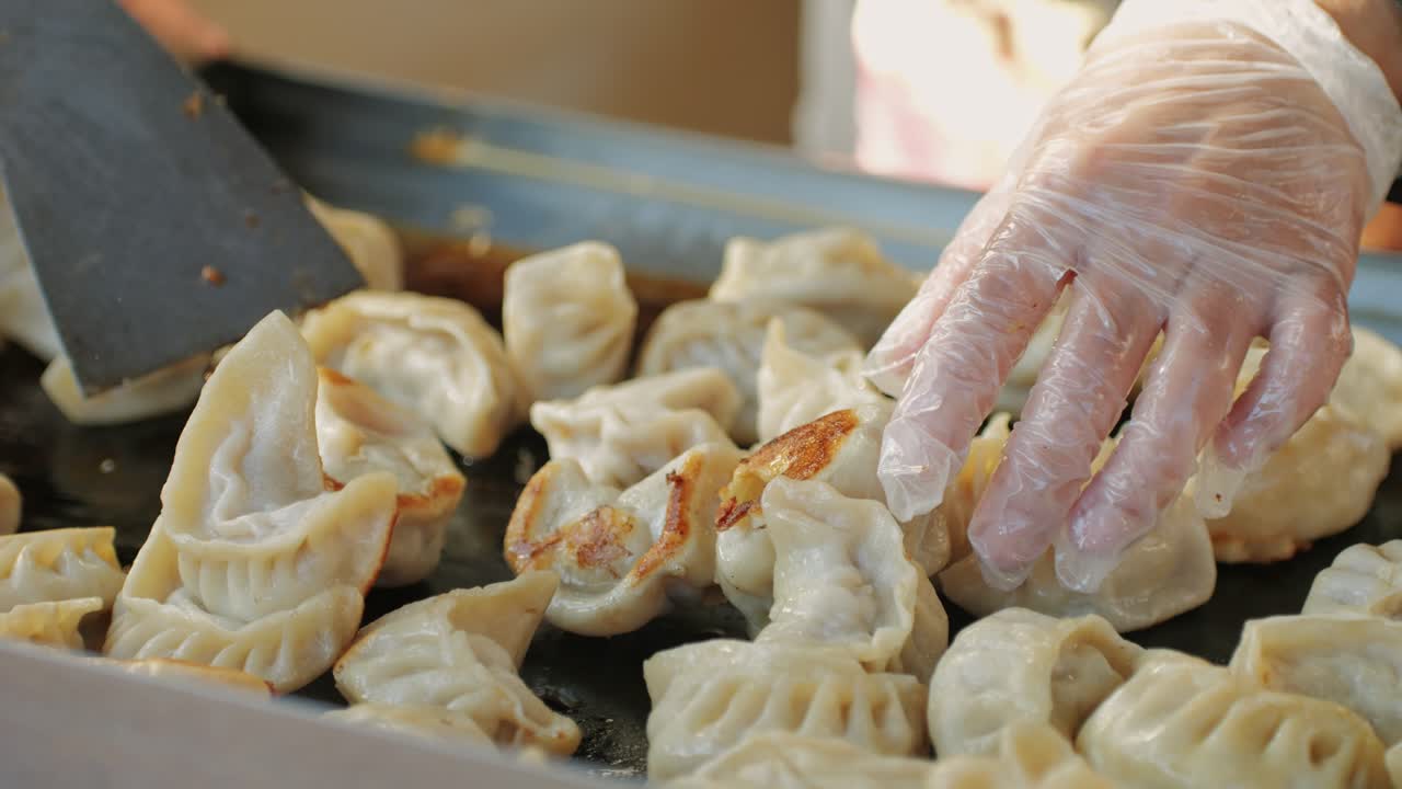 Cooking Chinese and Japanese Jiaozi or gyoza on boiling pan with oil close-up. Dumplings with meat pouring red sweet chilli sauce. Cooking at cafe, restaurant. Asian street food market outdoors.High quality 4k footage