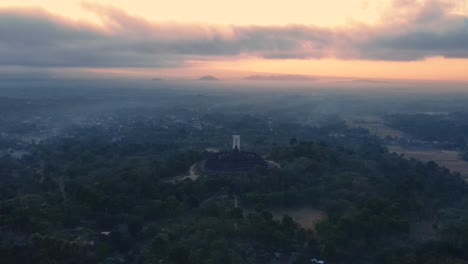 reveal drone shot of borobudur temple with magical light of sunrise in misty morning