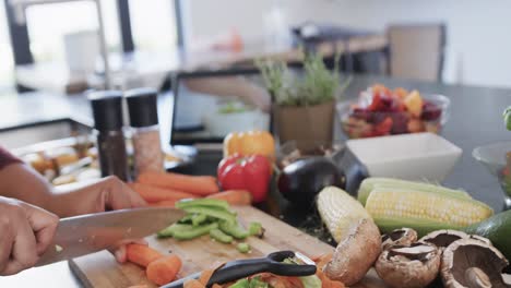 midsection of african american plus size woman chopping vegetables in kitchen, slow motion