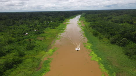 wide rising drone shot with a boat coming down the amazon river and the rainforest surrounding the river in peru