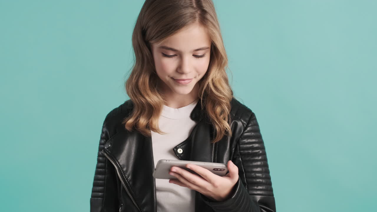 Teenage Caucasian girl in leather jacket watching videos on her smartphone.