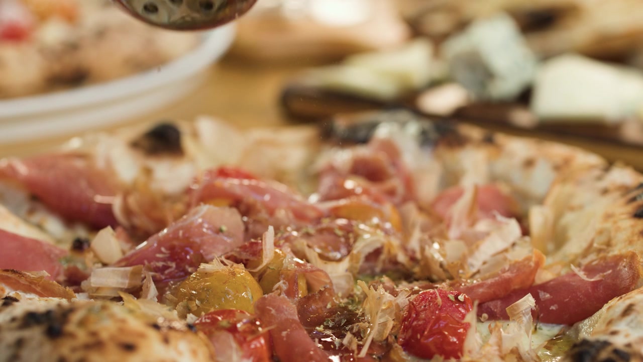 Primo piano di una mano che sparge spezie su una pizza gourmet fresca in un ambiente da ristorante