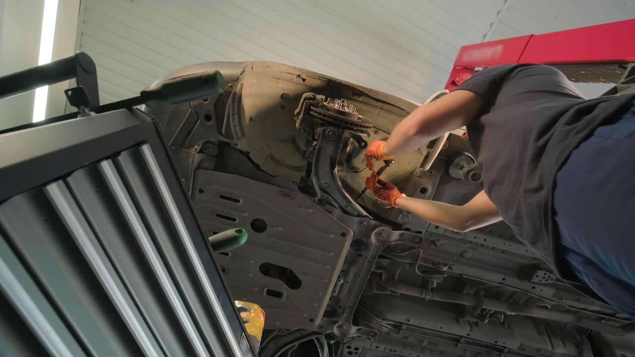 joven mecánico profesional que trabaja bajo el coche moderno levantado en el servicio de reparación de automóviles. servicio de automóviles, mantenimiento de reparación.