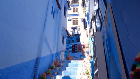 view looking up at tall blue apartments chefchaouen with tilt down to decorative pots on steps