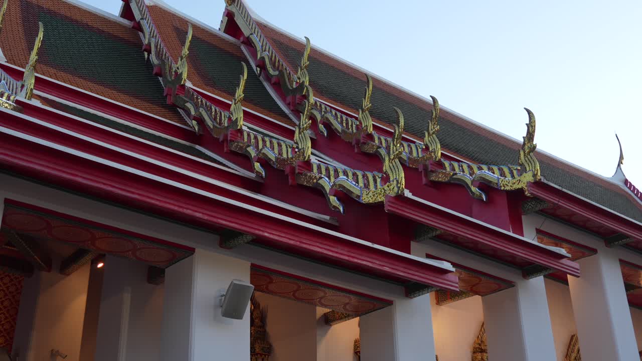 Ornate Wat Pho roof in Bangkok with vibrant red and green tiles, gilded chofahs and intricate decorative details against a clear sky, reflecting Thai spiritual heritage, slow motion reveal
