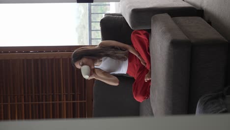 joven morena bebiendo té en su moderno sofá de apartamento