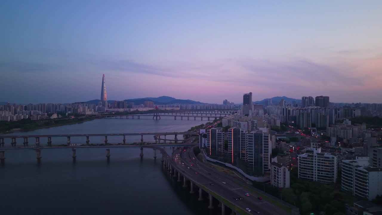 Prospettiva aerea all'ora blu sul traffico dell'autostrada Gangbyeonbuk-ro rivela la Lotte World Tower, tre ponti sul fiume Han e lo skyline degli appartamenti di Seul.