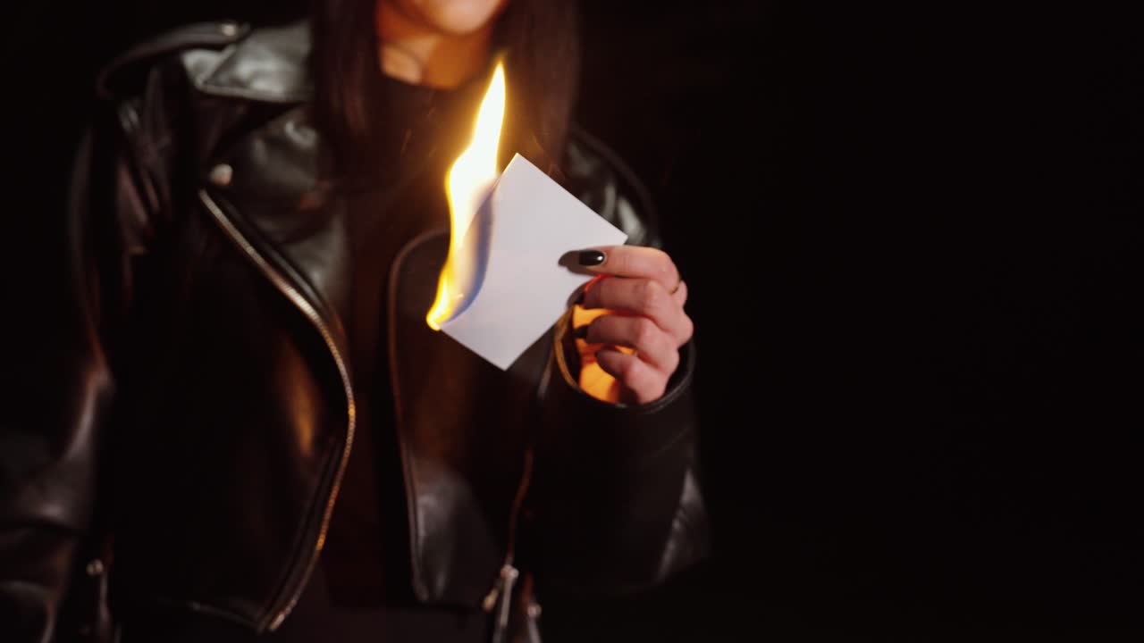 A woman holding a photograph as it burns in her hand, creating a symbolic, emotional, and cinematic moment against a dark background