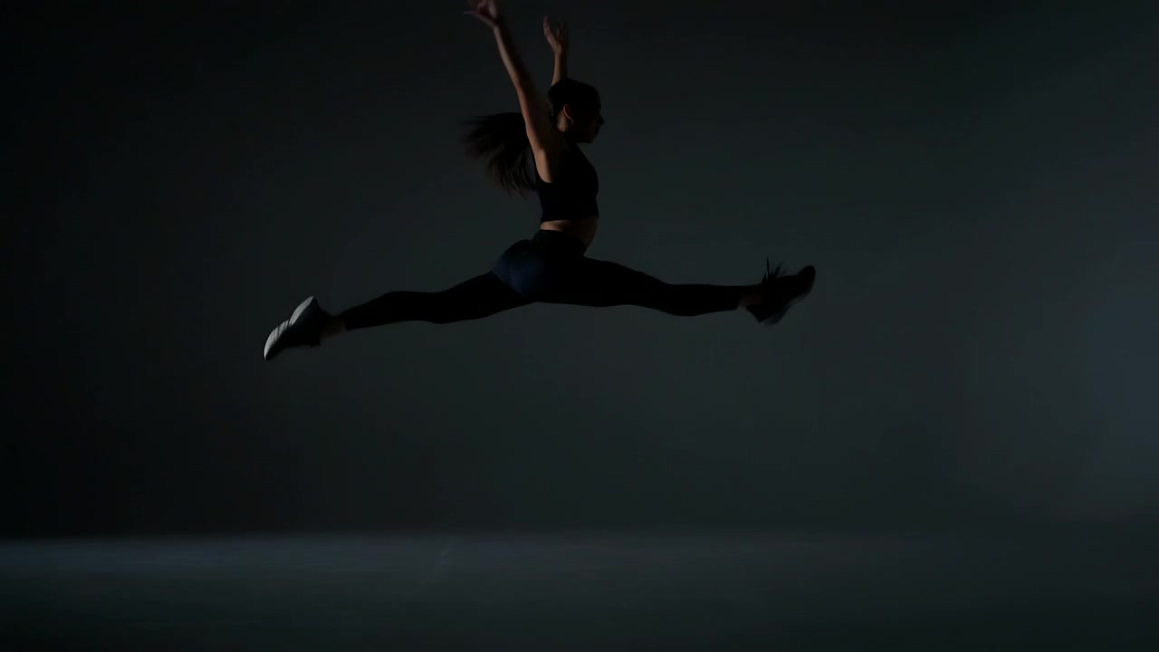 Ballerina in leggings che si lancia in un salto spaccata su un pavimento di studio illuminato di viola, durante le prove.