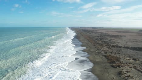 Aerial-descent-towards-breaking-waves-at-vast-Kaitorete-Spit-with-turquoiuse-colored-South-Pacific-Ocean