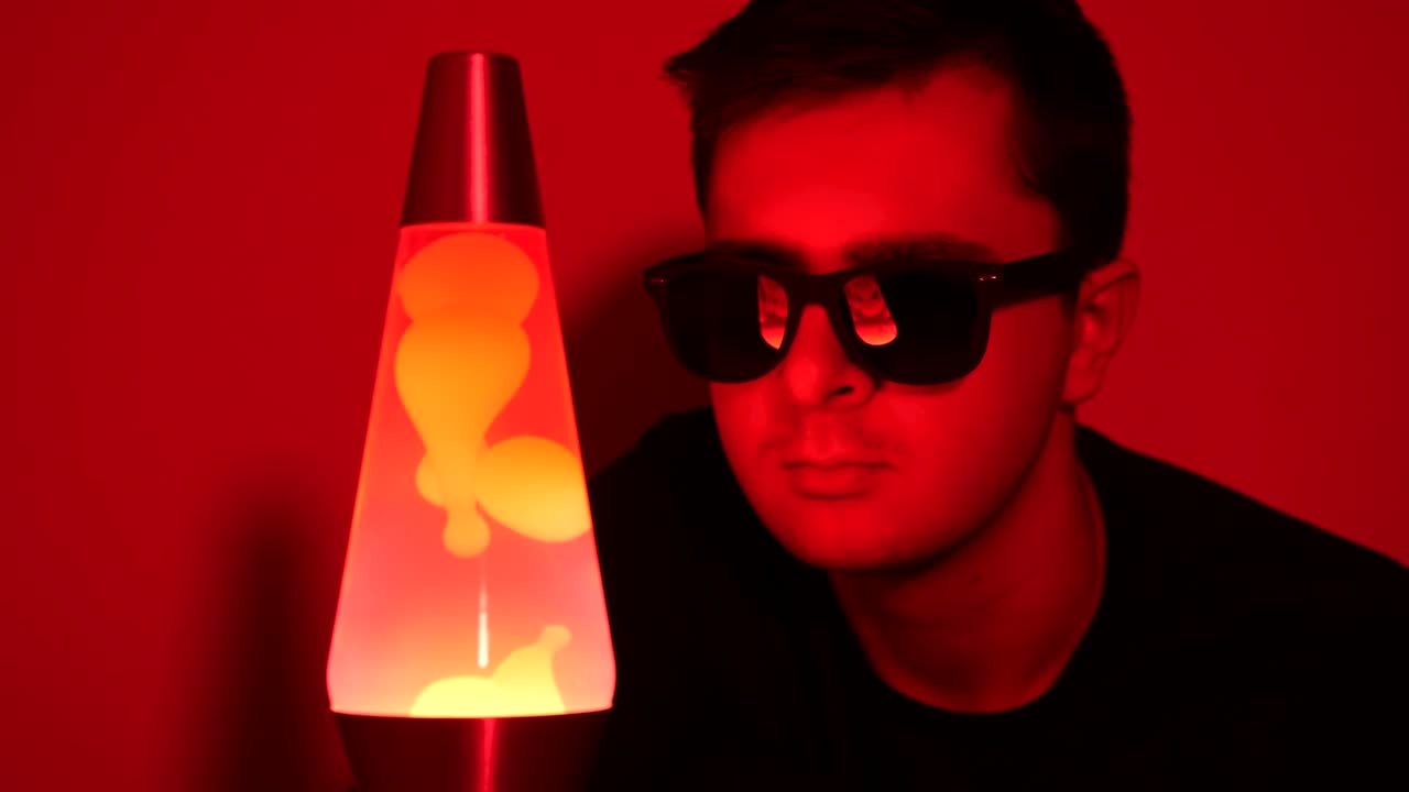 Close up of white yeen male looking at a red lava lamp while wearing shades