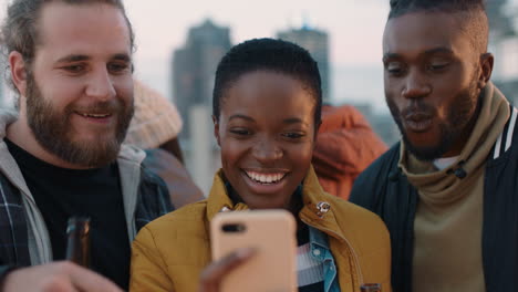 young-woman-using-smartphone-showing-group-of-diverse-friends-social-media-entertainment-enjoying-rooftop-party-at-sunset