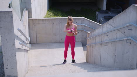 Blonde-girl-in-pink-sets-timer-on-watch-and-runs-up-stairs-outdoors