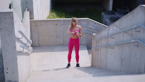 blonde girl in pink sets timer on watch and runs up stairs outdoors