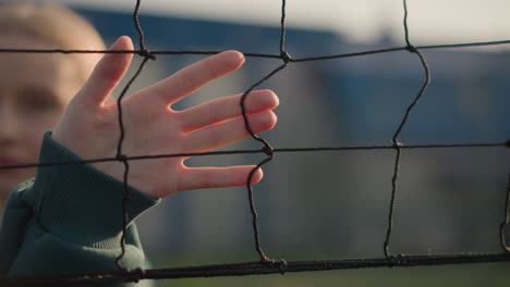 lady in green sweater gliding hand over volleyball net with soft sunlight illuminating her fingers, background slightly blurred, highlighting focus on hand movement and net texture