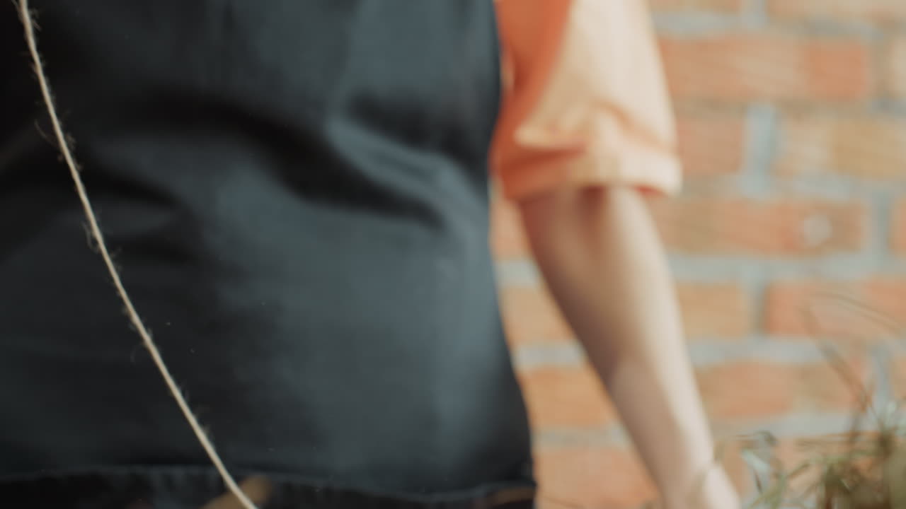 Florist in black apron holding spool of twine with both hands, preparing natural string for floral arrangement, focusing on handmade decoration, rustic workspace and creative preparation