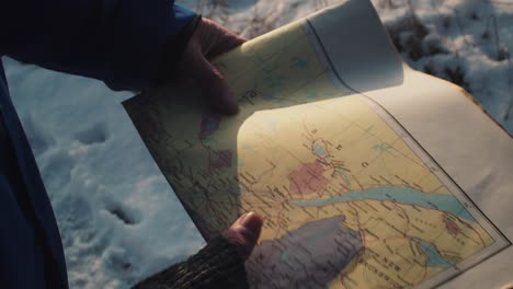 adulto sosteniendo un mapa en un suelo cubierto de nieve con luz solar golpeando un mapa de papel