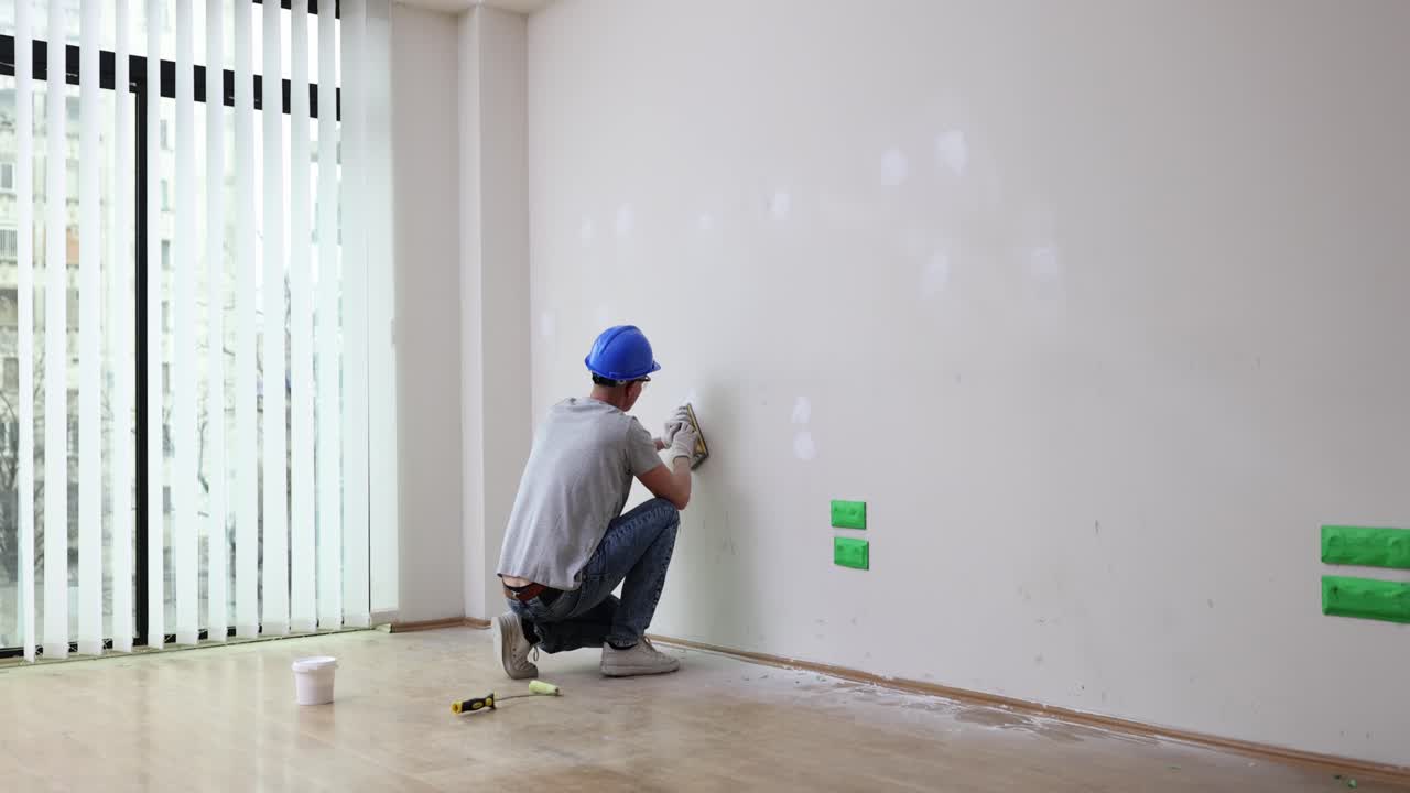 Repairman in helmet polishes white wall in restored room