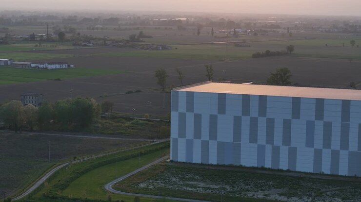 Logistik og forsyningskæde for et avanceret kølelagringsanlæg i Po-sletten, med automatiseret lager, kølelogistikdrift og et tilstødende solcelleanlæg på landbrugsjord, set fra et dronekredsløb ved solnedgang