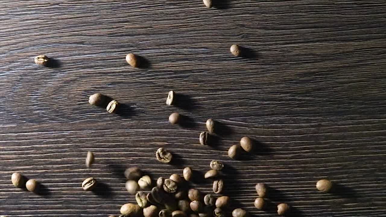 video animado de granos de café cayendo en cámara lenta. granos de cafe arabica tostados sobre un fondo de madera.