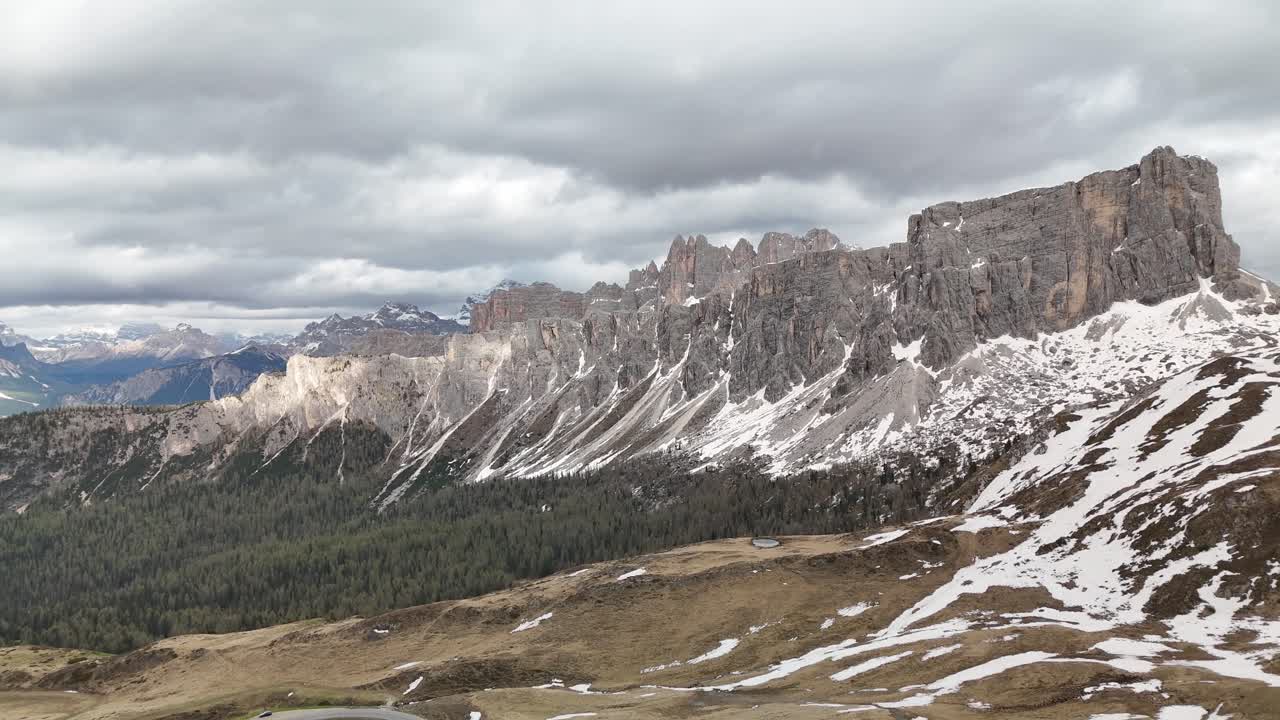 Aerial drone flight toward a distinctive steep rock mountain formation at Passo Giau, Dolomites, Italy. Fresh snow from last night and drifting clouds create a dramatic alpine scene