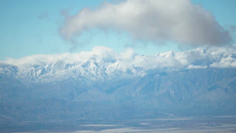 fluffy-clouds-move-over-snow-covered-mountains,-creating-beautiful-shadows-in-the-soft-morning-light