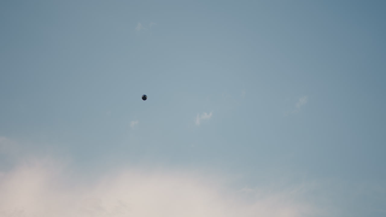 Paraglider floats gracefully across wide open sky framed by wispy clouds and clear blue background, capturing sense of freedom and adventure in peaceful daytime atmosphere