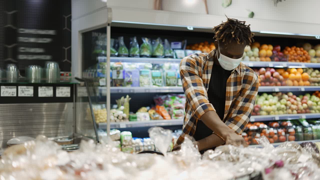 마스크를  ⁇ 고 있는 남자가 신선한 식품 섹션에서 과일과 채소를 선택하고 있습니다.