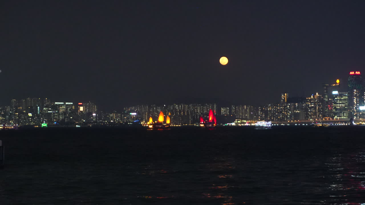 밤에 빅토리아 항구를 가로지르는 빛나는 붉은 돛을 단 홍콩의 전통 중국식 정크선.