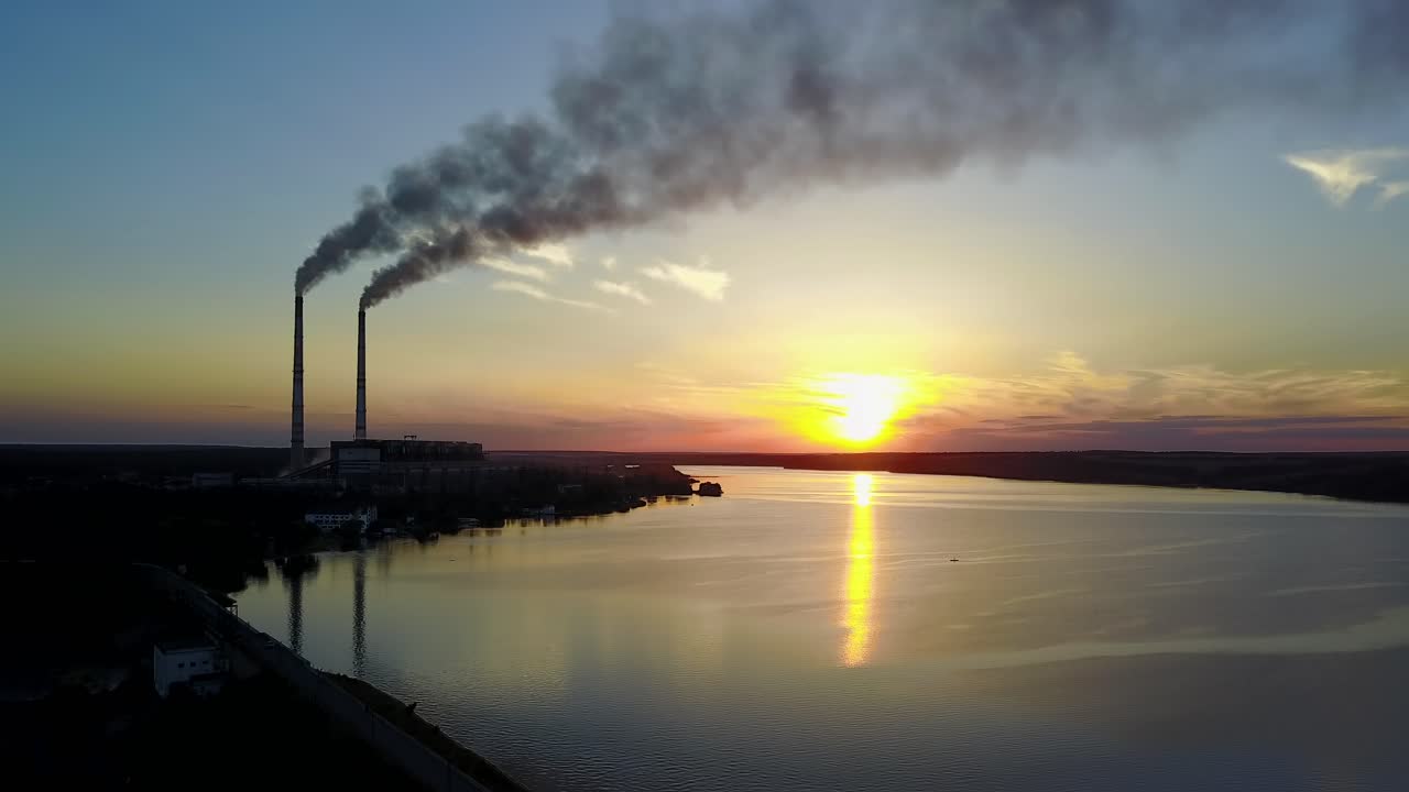 Pollution Of The Environment By The Plant. Industrial evening landscape with factory pipes and river at sunset