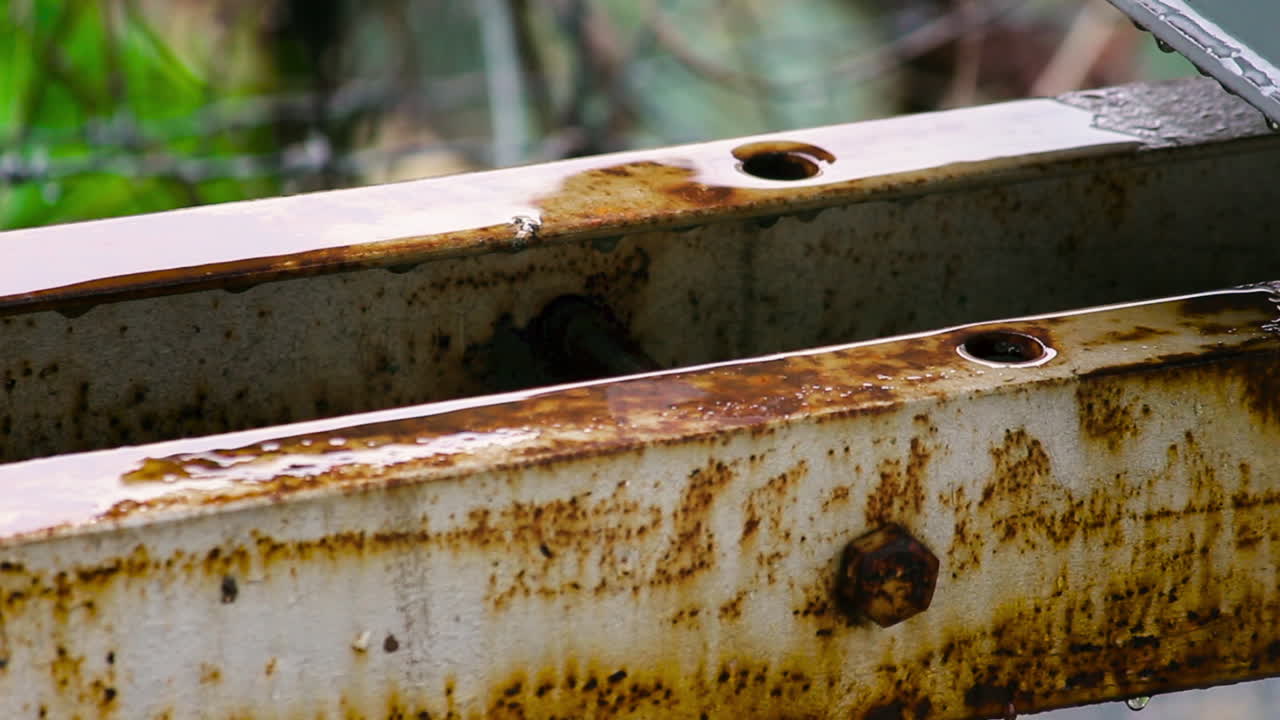Detailed close-up of rusty metal beam getting wet in rain. Perfect for concepts of decay, weather impact, corrosion and industrial texture