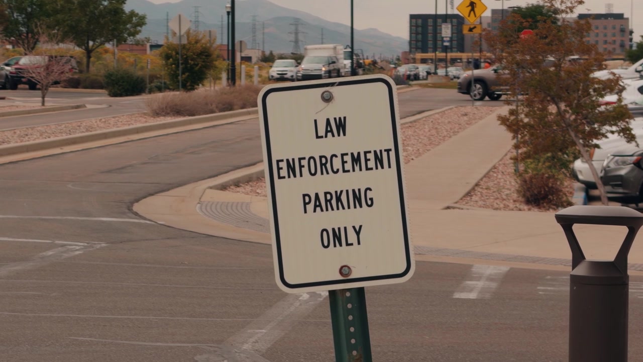 Static focus on a parking restriction sign while cars pass out of focus behind it.