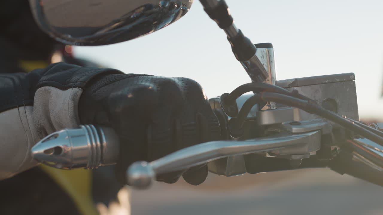 Close up of biker hand gripping throttle on motorcycle handle, wearing leather glove, mirror reflecting city scene in soft daylight, emphasizing control, strength, speed, and freedom of urban riding