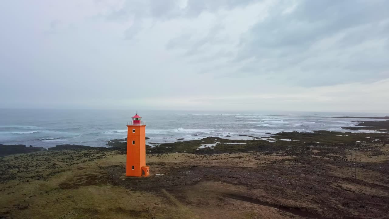 el faro naranja se encuentra en contraste con una costa rocosa y temperamental en islandia.