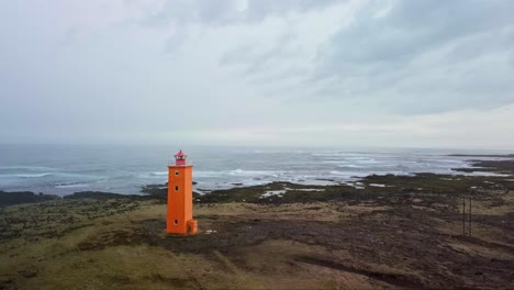 oranje vuurtoren staat in contrast tegenover een rotsachtige, humeurige kustlijn in ijsland