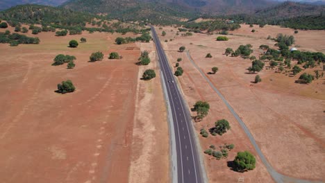 Vista-Aérea-De-Un-Coche-Conduciendo-Por-Un-Largo-Camino-De-Tierra-En-Un-Paisaje-Abierto