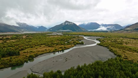 beech forest lines riverbanks with meandering river on cloudy day in lowlands of south island