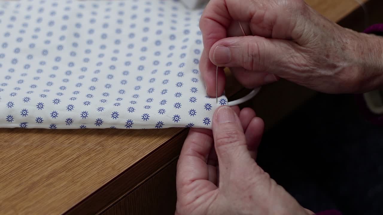 Close-up of elderly hands sewing string for handmade covid19 prevention mask